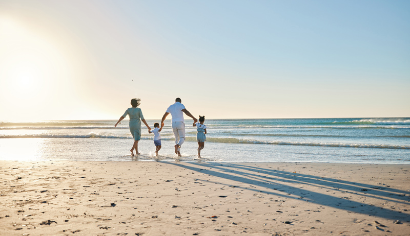 A happy family of four runs toward the ocean on a sunny beach, symbolizing connection, healing, and growth through family therapy. The warm sunlight and peaceful waves represent a journey toward stronger relationships, emotional well-being, and positive communication.