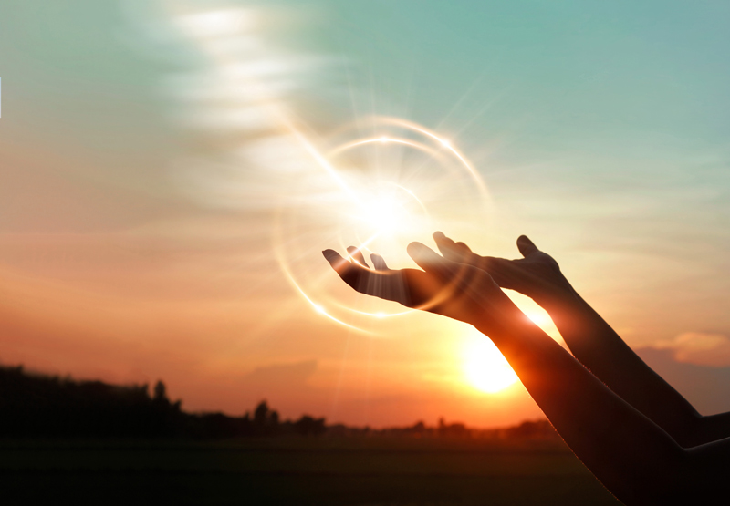 Open hands reach toward glowing light at sunset, symbolizing healing, renewal, and inner strength through PTSD therapy. The warm sky and radiant energy represent hope, emotional recovery, and the journey toward mental well-being.